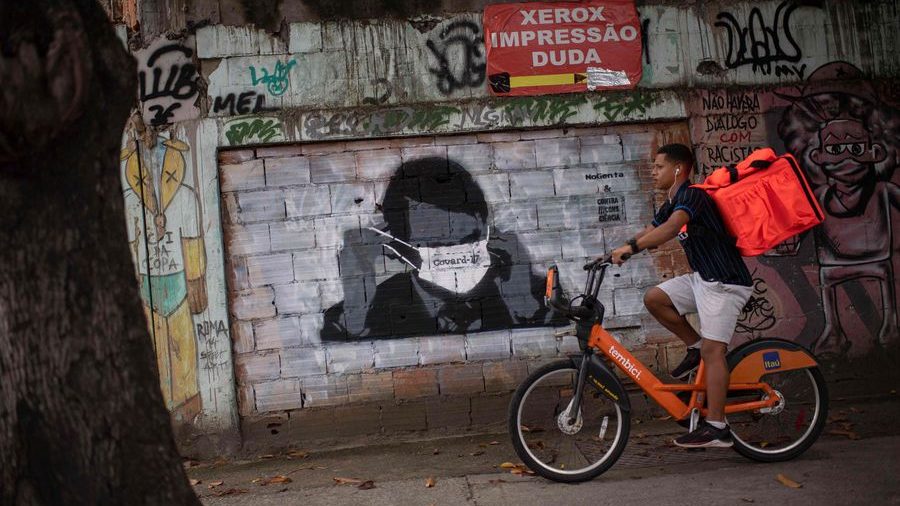 man on bike in front of street art with spanish writing and a facemask graffiti